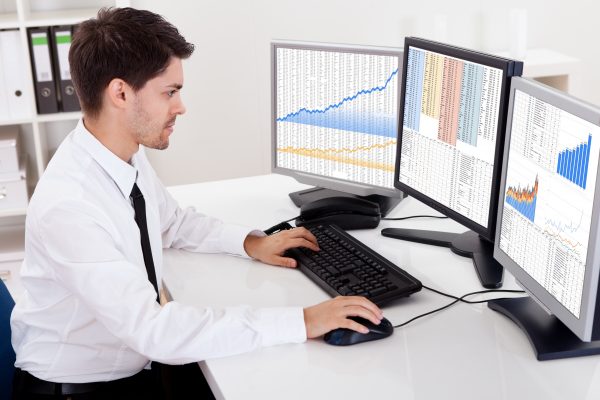 Stock broker trading in a bull market Over the shoulder view of the computer screens of a stock broker trading in a bull market showing ascending graphs